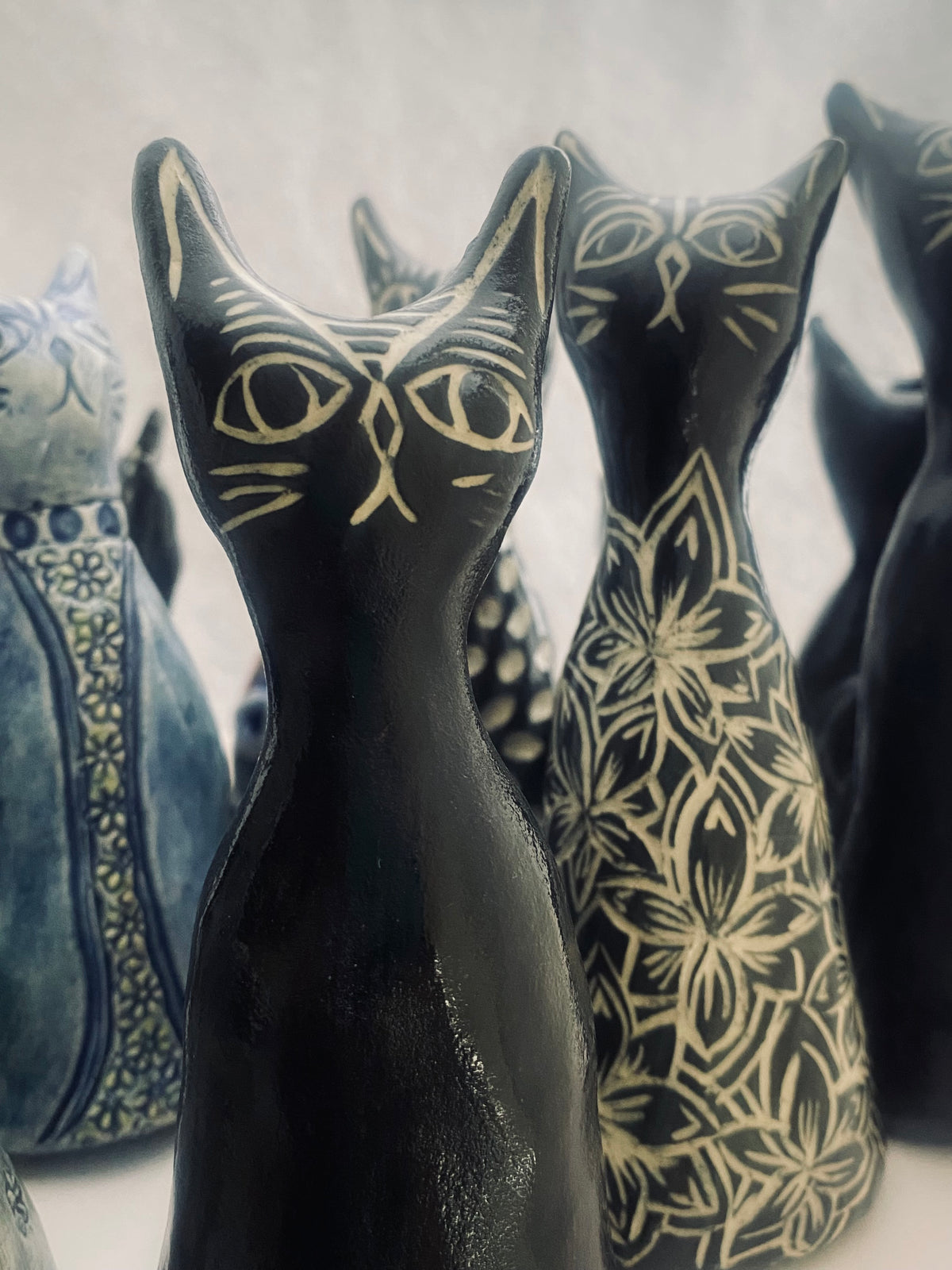A gathering of hand-sculpted stoneware cats by Mary Egan, with dark glazes, cream whiskers and floral decoration.